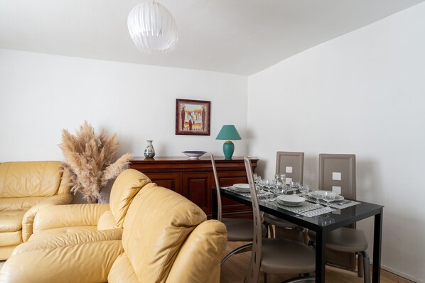 A dining area with a table set for four, a sofa, and a decorative vase.