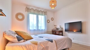 Une chambre à coucher avec un lit, un bureau, une télévision et une fenêtre avec des rideaux.