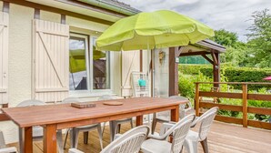 A wooden deck with a table and chairs, a green umbrella, and a white birdcage.