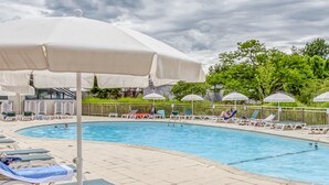 A swimming pool with lounge chairs and umbrellas, surrounded by greenery and a fence.