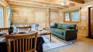 A wooden cabin interior with a dining area, a sofa, and a window. - 2 bedroom accommodation in Killin, near Crianlarich (Killin, near Crianlarich)