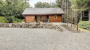A rustic cabin with a stone wall entrance, wooden exterior, and a gravel driveway. - 2 bedroom accommodation in Killin, near Crianlarich (Killin, near Crianlarich)