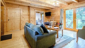 A wooden cabin interior with a sofa, dining table, and a television. - 2 bedroom accommodation in Killin, near Crianlarich (Killin, near Crianlarich)