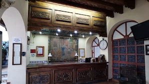 Een receptie met een houten balie, een groot schilderij en een klok aan de muur.
