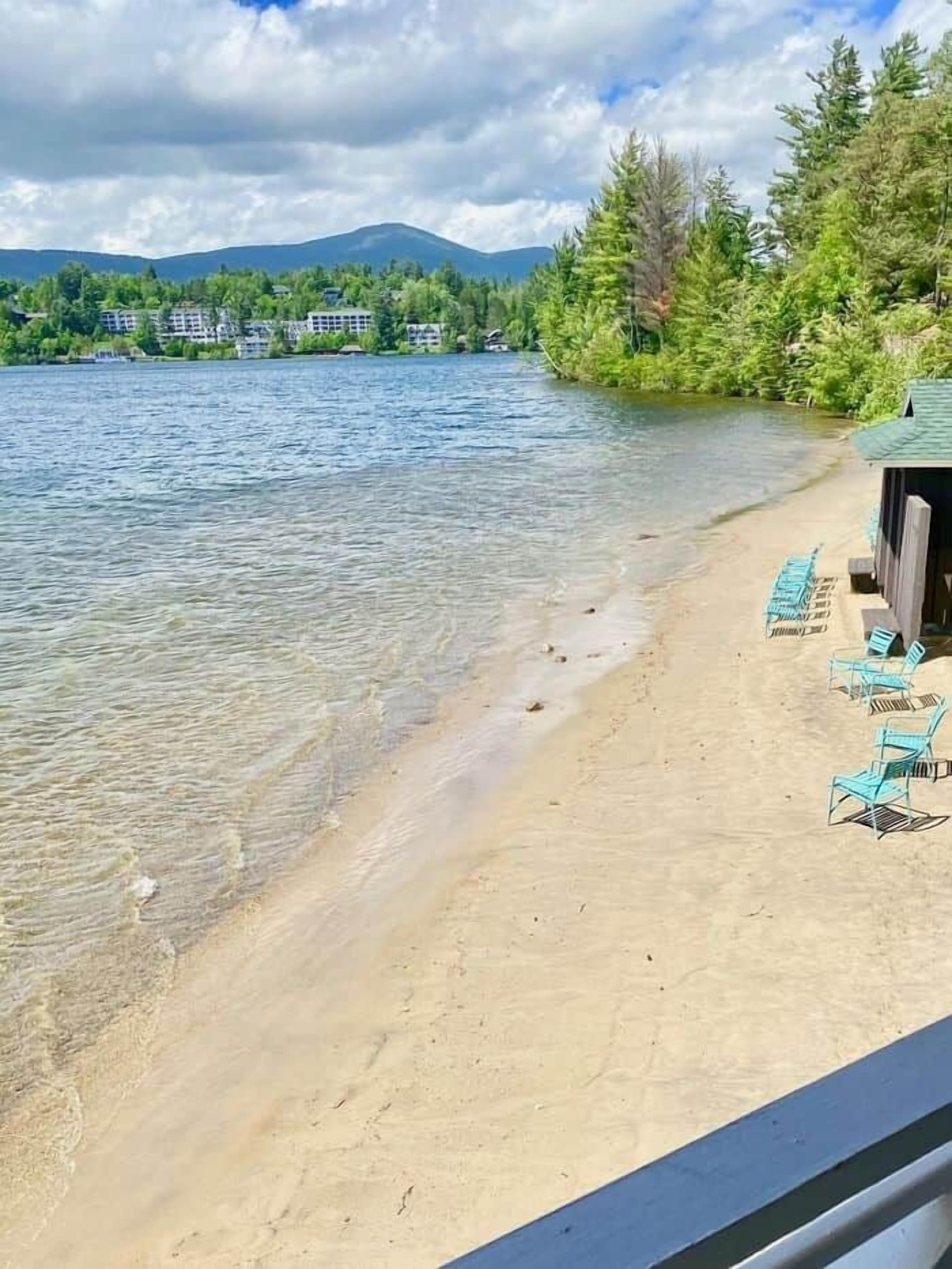 Une vue sur le lac, avec une plage de sable, des chaises longues et une zone boisée.