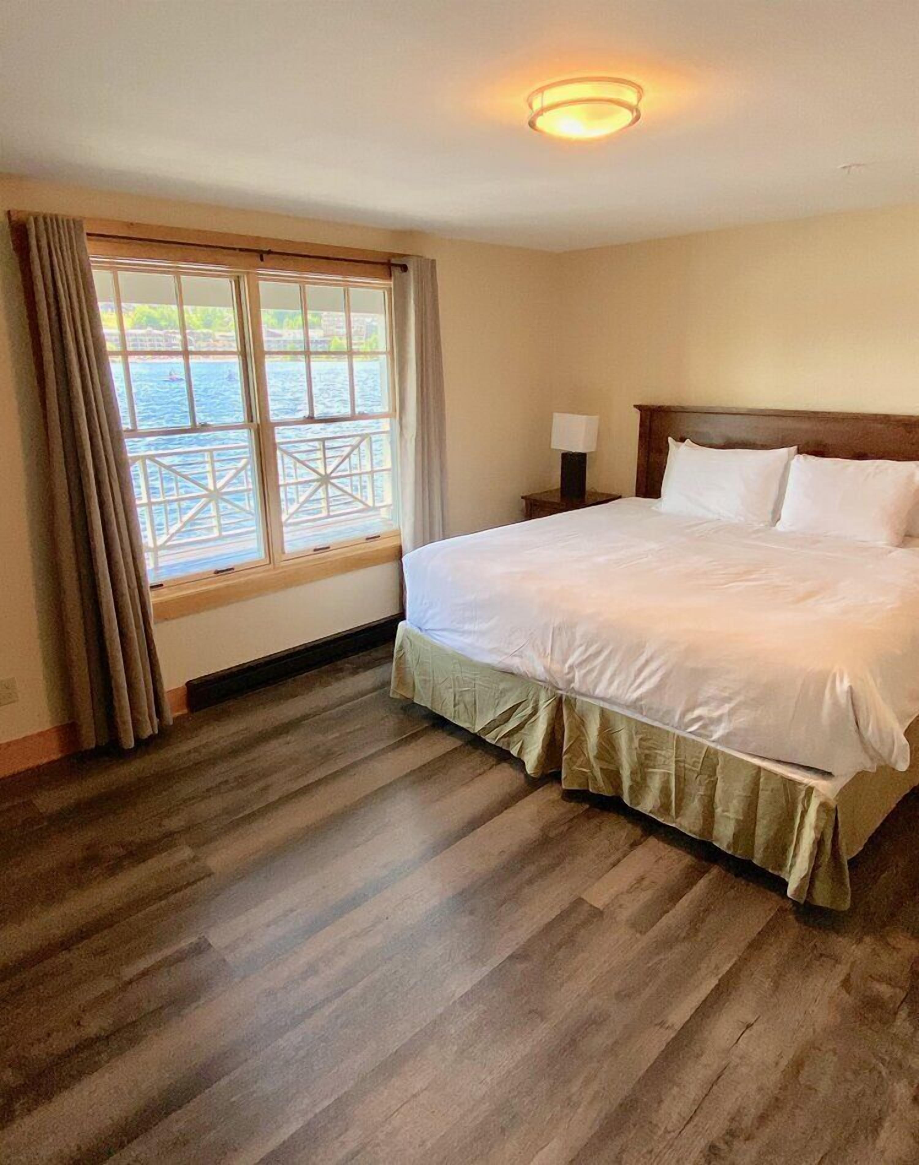 Une chambre d’hôtel avec un grand lit, une table de chevet, une lampe et une fenêtre donnant sur l’eau.