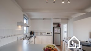 Una cocina moderna con armarios blancos, estufa a gas, microondas y refrigerador. Hay un cuenco con fruta sobre la encimera.