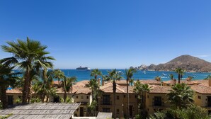 A coastal view with a cruise ship in the distance, palm trees, and buildings with red-tiled roofs. - Cabo Dream Stay-4BR Oceanview at Hacienda Beach Club can be rented as 2-3 bedrm (Cabo San Lucas)
