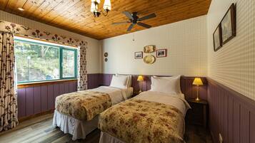 A room with two beds, wooden ceiling, floral curtains, and a window with a view of greenery.