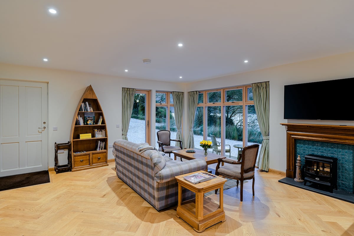 Una sala de estar con sofá, sillas, chimenea, estantería y ventanas amplias.