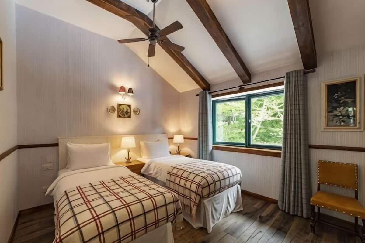 A room with two beds, a ceiling fan, a window with a view, and a bench.