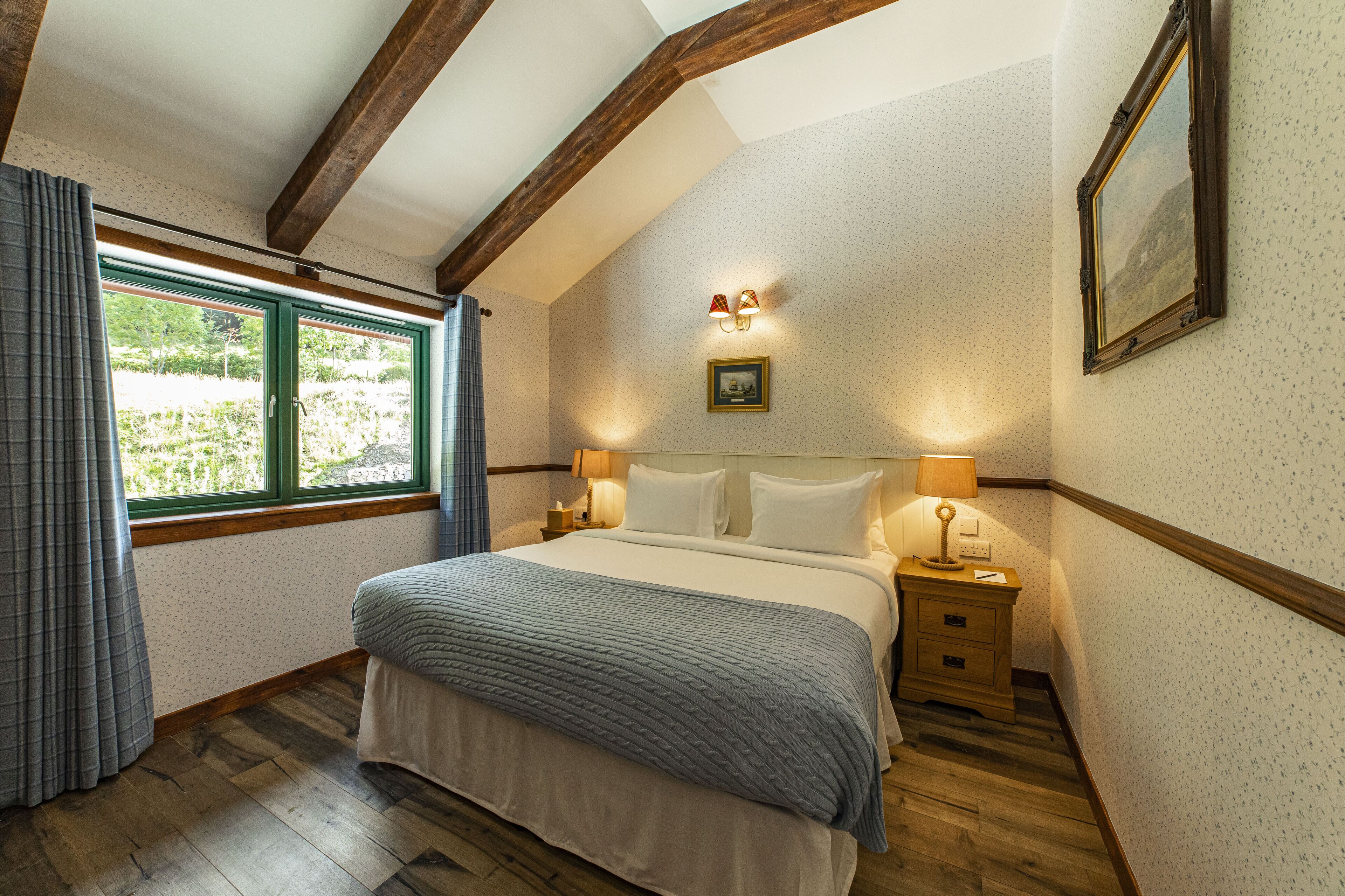 A bedroom with a bed, nightstands, a window with curtains, a wall-mounted lamp, and a framed picture.