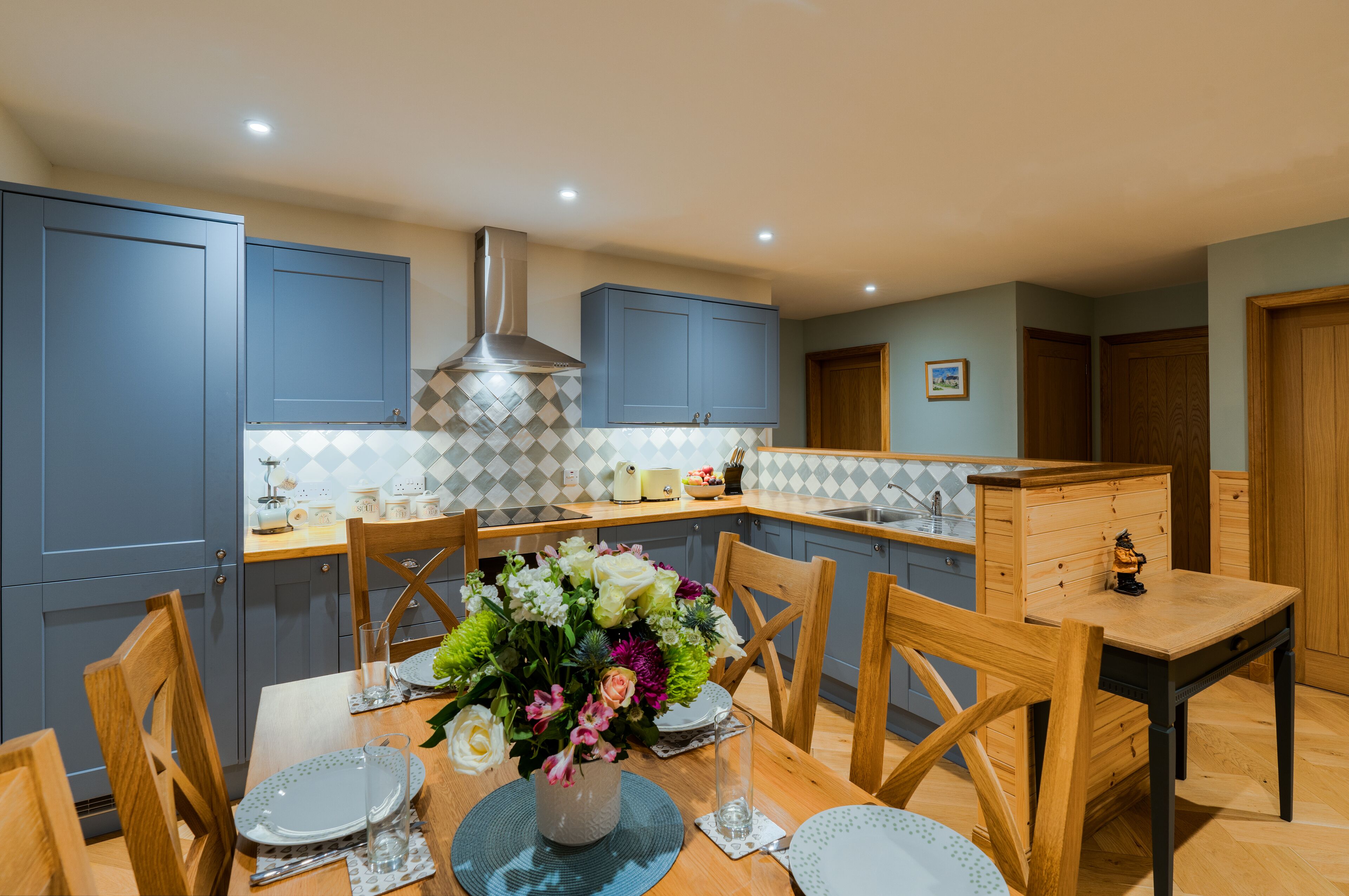 A modern kitchen with blue cabinets, a central island, and a dining table set for four.