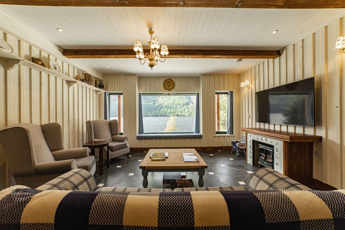 Una sala de estar acogedora con chimenea, asientos cómodos, televisor y un ventanal con vistas panorámicas.