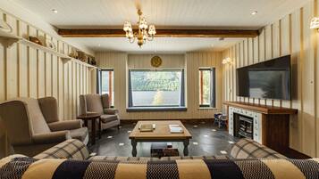 A cozy living room with a fireplace, comfortable seating, a television, and a large window offering a scenic view.