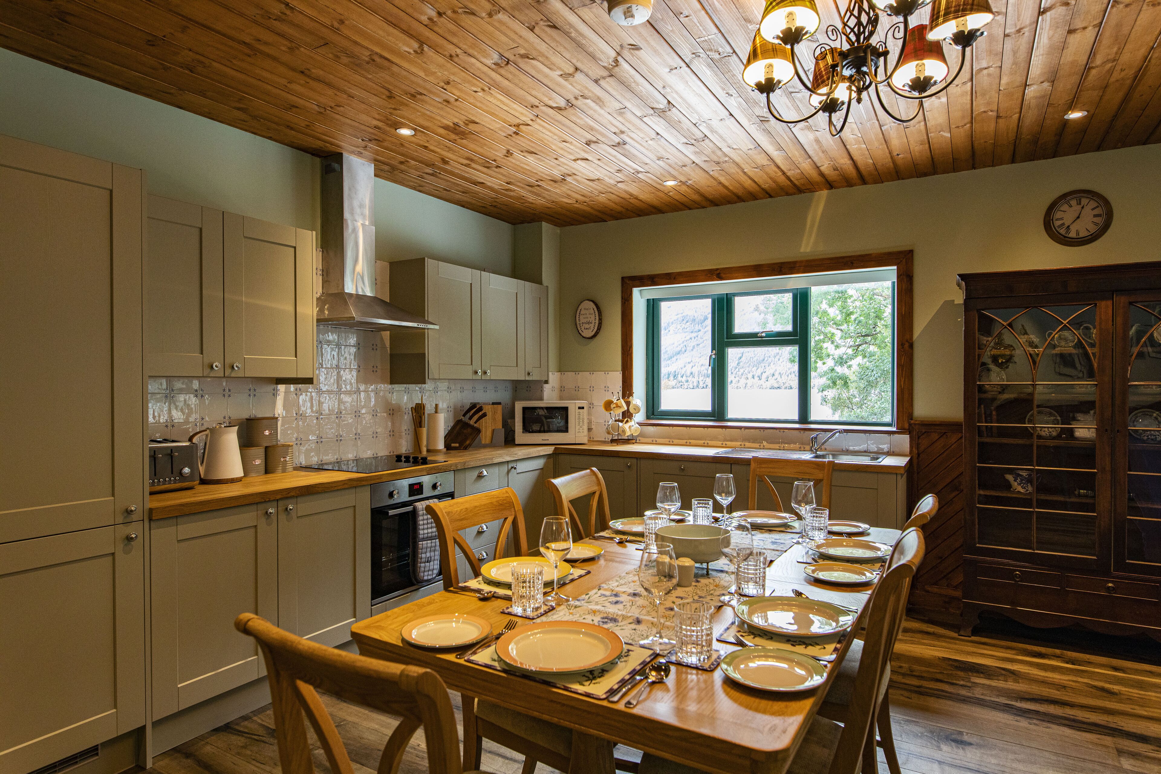 Una cocina bien iluminada con armarios de madera, una mesa de comedor lista para seis personas y un ventanal que proporciona luz natural.