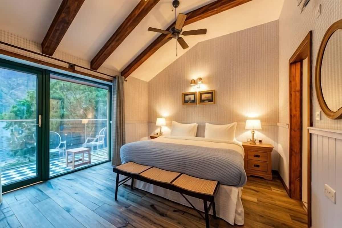 Un dormitorio con cama, mesitas de noche, un banco, ventilador de techo y puerta corrediza de vidrio que da a un área exterior.
