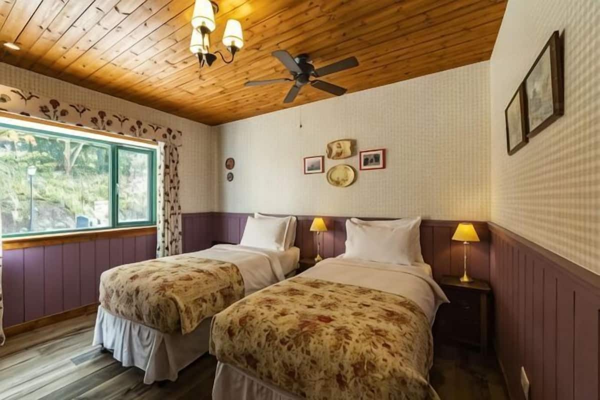 Una habitación con dos camas, un ventilador de techo, una ventana con cortinas y un reloj de pared.