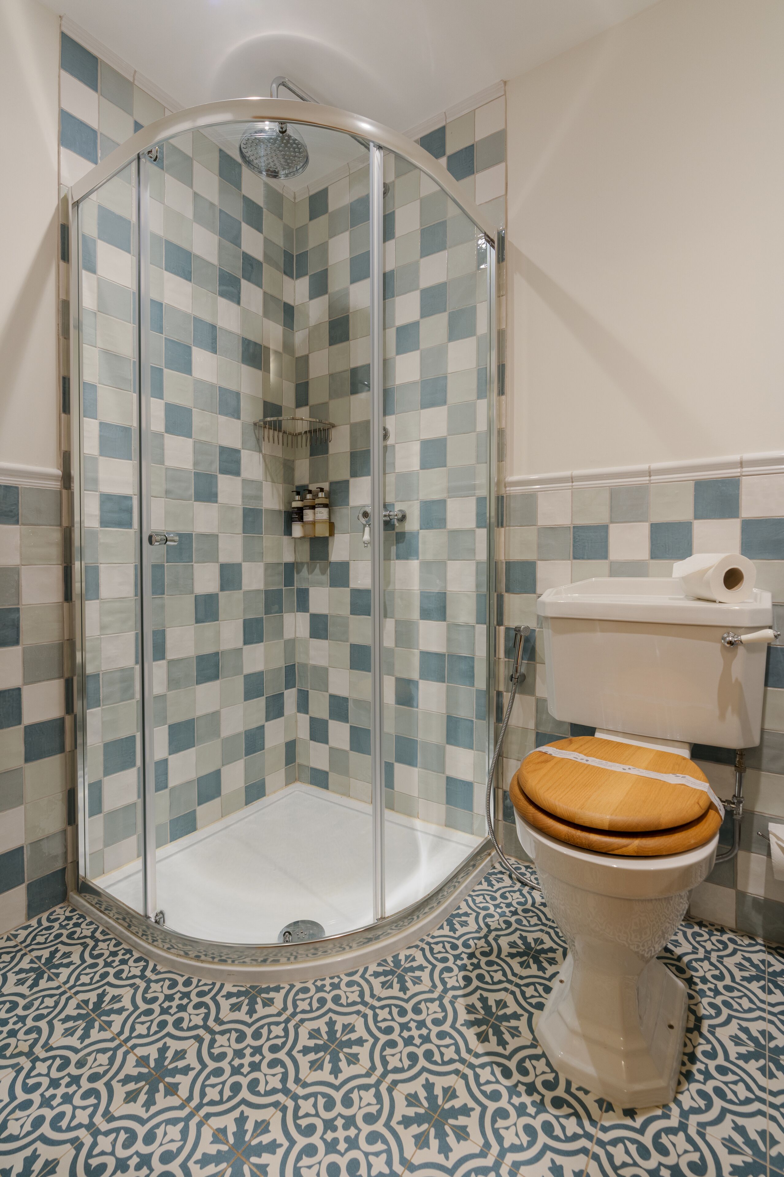 Een badkamer met een vloer van zwart-wit betegelde tegels, een douchecabine van glas en een toilet met houten zitting.