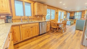 A spacious kitchen with wooden cabinetry, a stainless steel dishwasher, and a dining area with a wooden table and chairs. - Fall Colors, ATV Trails & Lake Fishing Retreat (Crystal Falls)