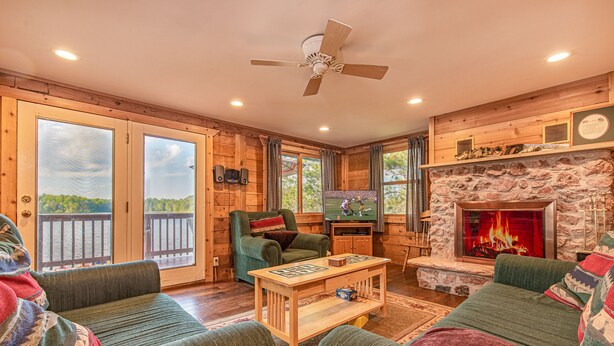 A cozy cabin interior with a fireplace, wooden walls, a green armchair, and a view of the outdoors. - Fall Colors, ATV Trails & Lake Fishing Retreat (Crystal Falls)