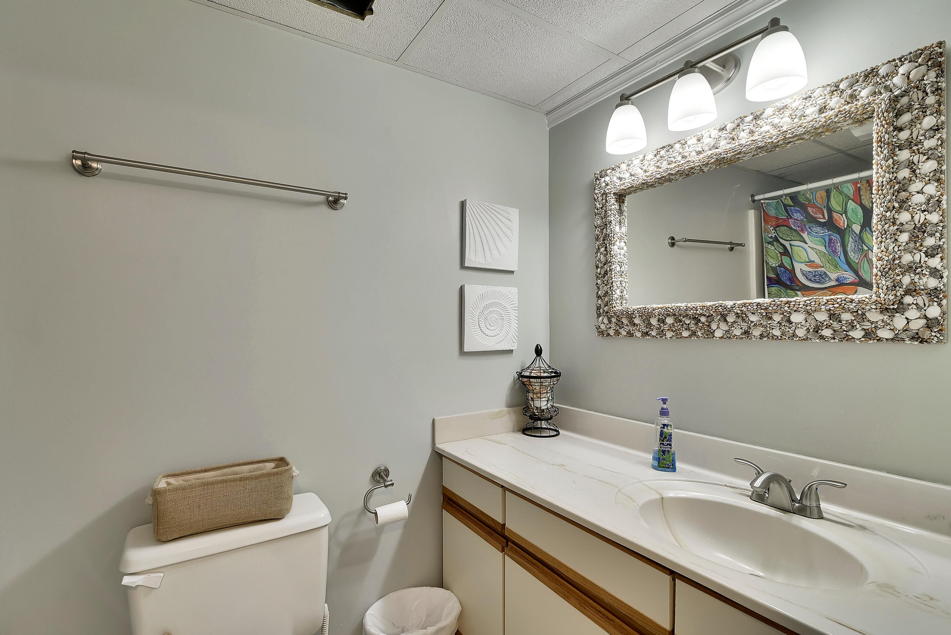 Un baño con inodoro, lavabo, espejo, toallero y un adorno de pared.