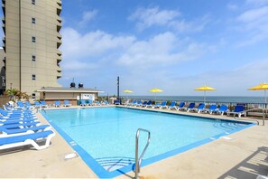 A swimming pool with blue lounge chairs and yellow umbrellas, a building with a flat roof, and a clear sky. - DAILY ACTIVITIES & LINENS INCLUDED*!! Direct Oceanfront  2  bedroom, 2 bath with an open den (set up as dining room). (Ocean City)