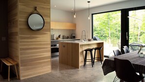 Une cuisine moderne avec des meubles en bois, un îlot central doté de tabourets de bar et une grande fenêtre offrant une vue sur la verdure.