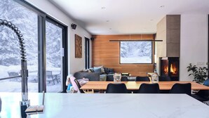 Un salon moderne doté d’une cheminée, de grandes fenêtres et d’un coin repas.