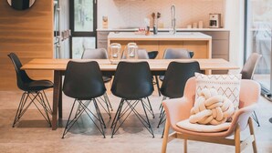 Un espace repas moderne avec une table en bois, des chaises noires et une cuisine en arrière-plan.