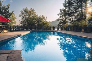 Una piscina con muelle de madera, rodeada de árboles y una montaña al fondo.