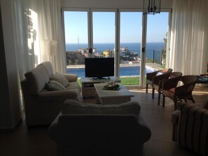 Relax in this stylish living room with a sofa set and flat-screen TV, offering a panoramic view of the sea.