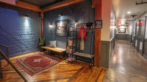 A hallway with a wooden bench, a red rug, a wall-mounted shelf with a red jacket, and a framed picture on the wall. - The Lofts at Downtown Salem (Salem)