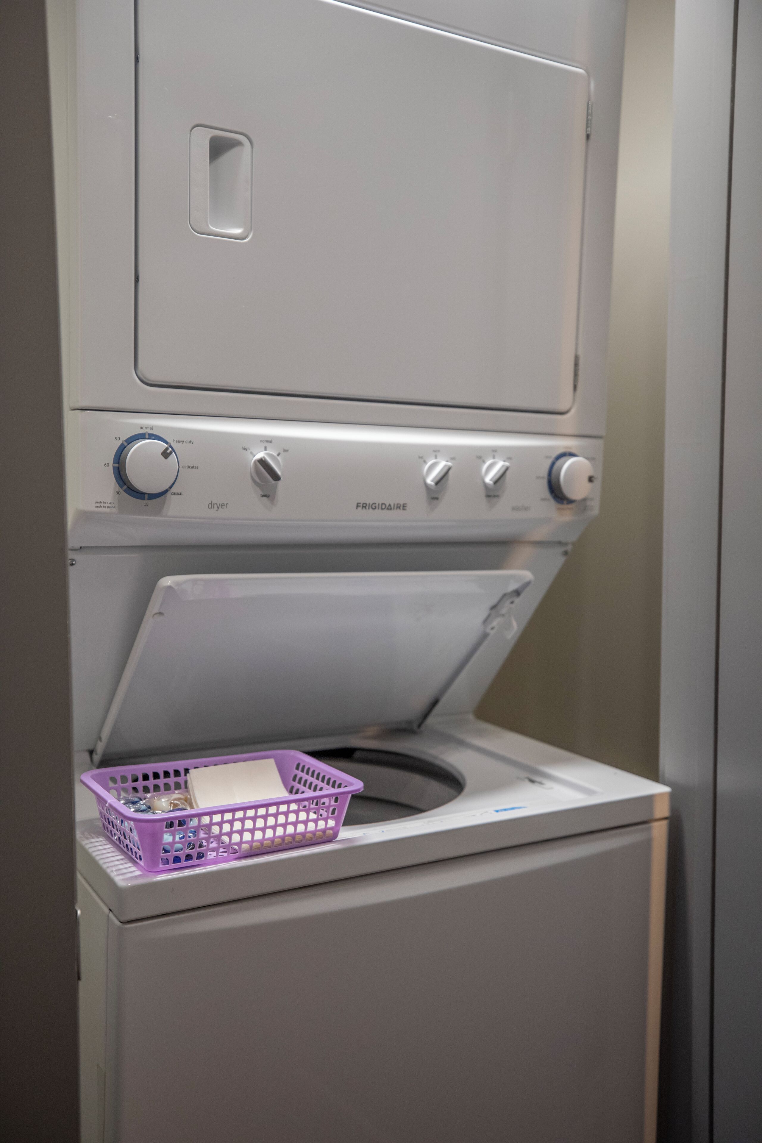 A compact washer and dryer unit with a purple basket on top.