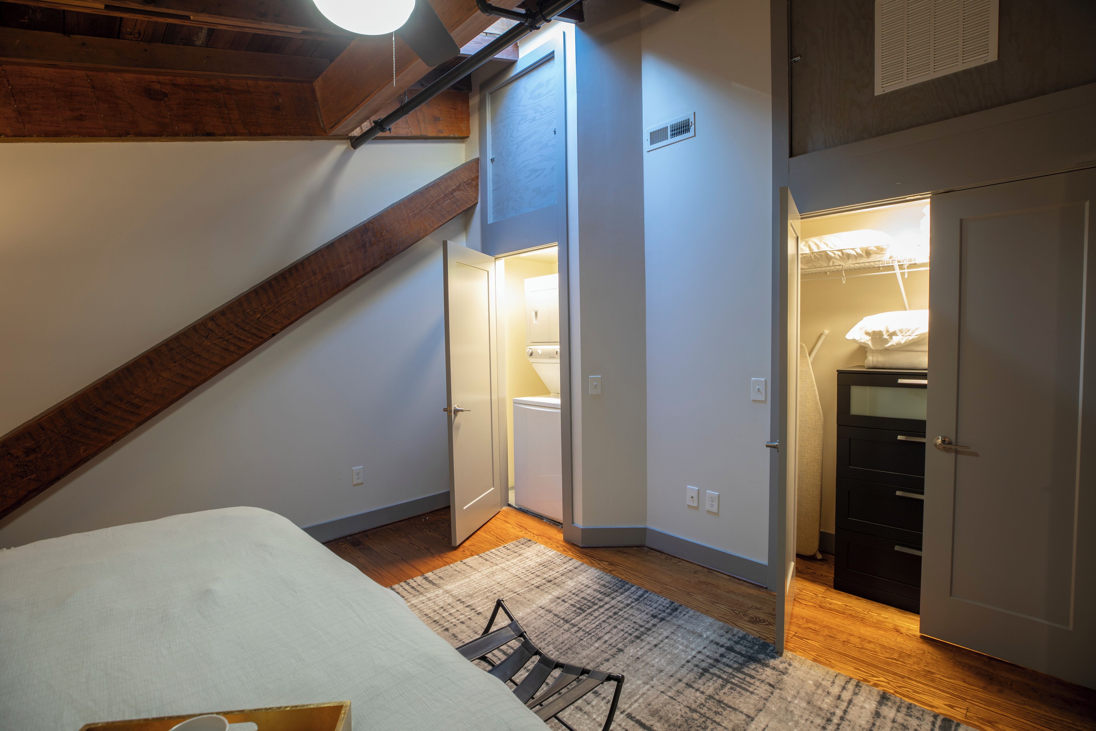 Una camera da letto con un letto, soffitto in legno, parete bianca, una porta e un armadio.