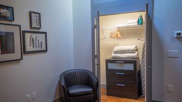 A room with a black leather chair, a wooden floor, a closet with hanging clothes, and framed pictures on the wall.