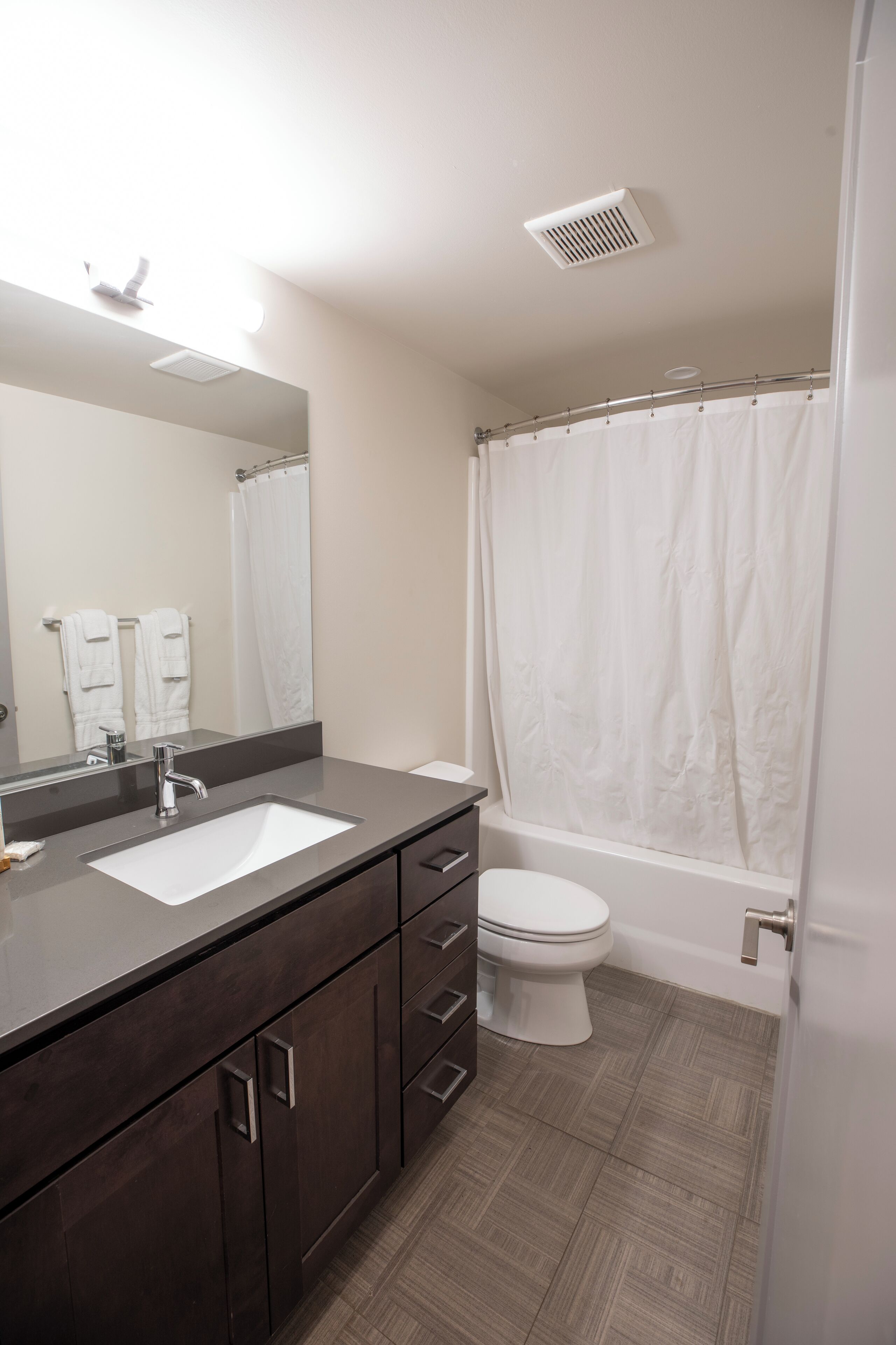 A bathroom with a dark wood vanity, a white sink, a mirror, a white toilet, and a shower with a white curtain.