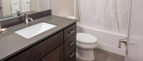 A bathroom with a dark wood vanity, a white sink, a mirror, a white toilet, and a shower with a white curtain.