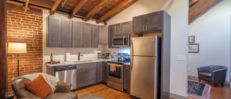 A modern kitchen with stainless steel appliances, wooden beams, and a cozy seating area with a leather couch and ottoman.