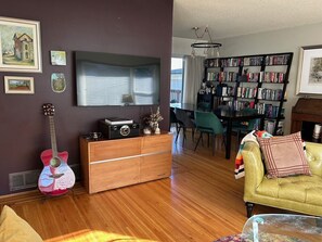 A living room with a wooden cabinet, a guitar, a sofa, and a bookshelf. - Great Family Home in Lynn Valley (North Vancouver)