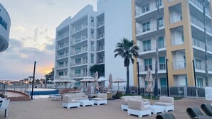 Un hotel con varios pisos, zonas de estar al aire libre con sombrillas y piscina.