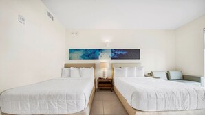 Habitación de hotel con dos camas, una mesita de noche con lámpara y dos obras de arte abstracto en la pared.