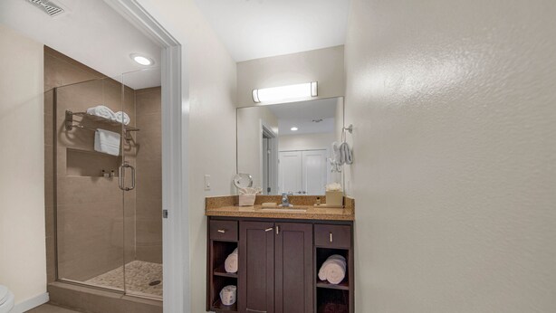 A bathroom with a glass-enclosed shower, a vanity with a mirror, and shelves for towels. - Upper Level  Unit + Access to Infinity Pool (South Padre Island)
