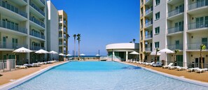 A hotel pool area with sun loungers and umbrellas, surrounded by multi-story buildings with balconies. - Upper Level  Unit + Access to Infinity Pool (South Padre Island)