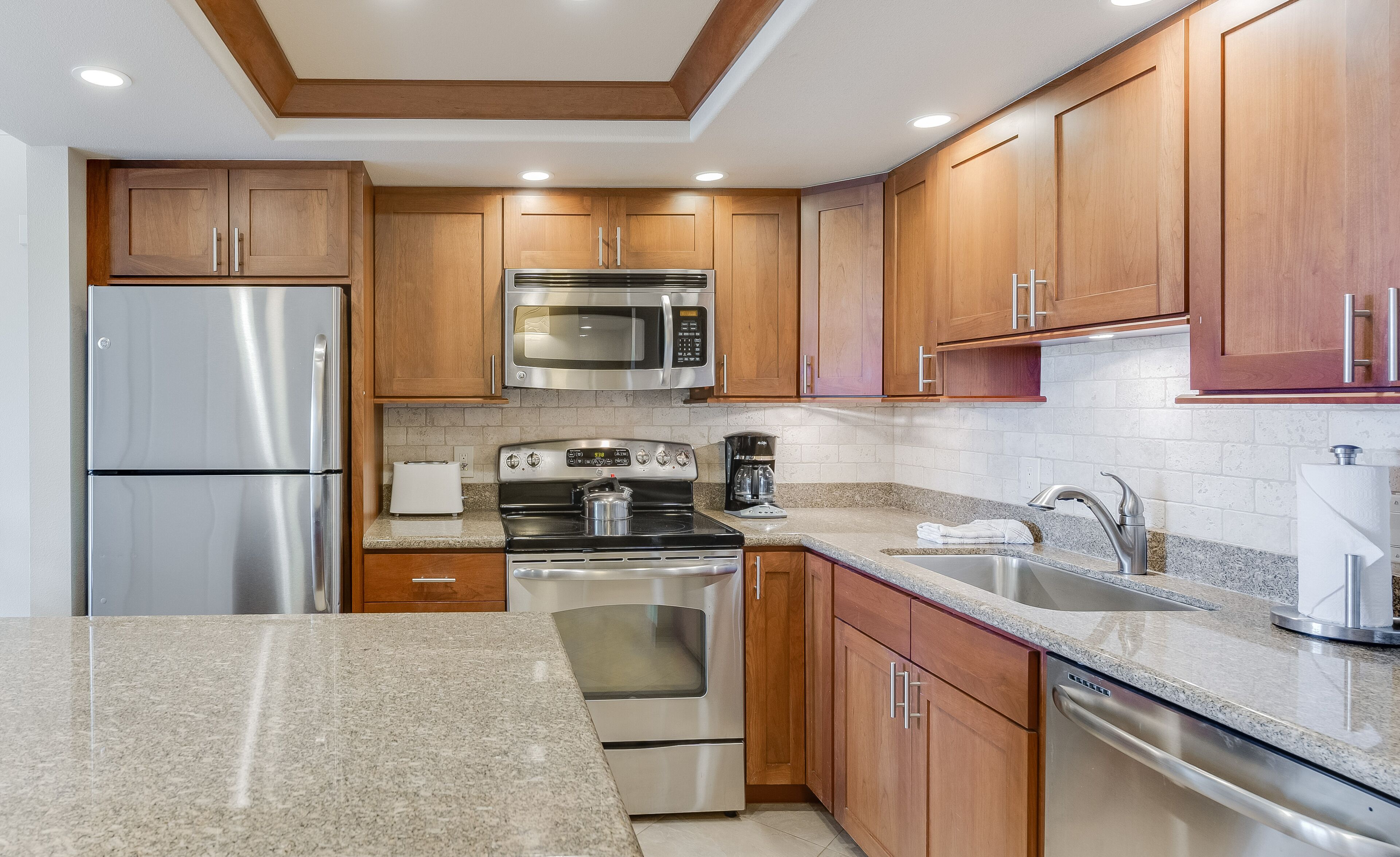 A modern kitchen with stainless steel appliances, wooden cabinets, granite countertops, and a built-in oven.