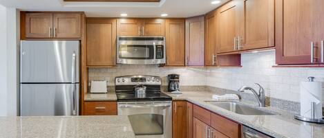 A modern kitchen with stainless steel appliances, wooden cabinets, granite countertops, and a built-in oven.