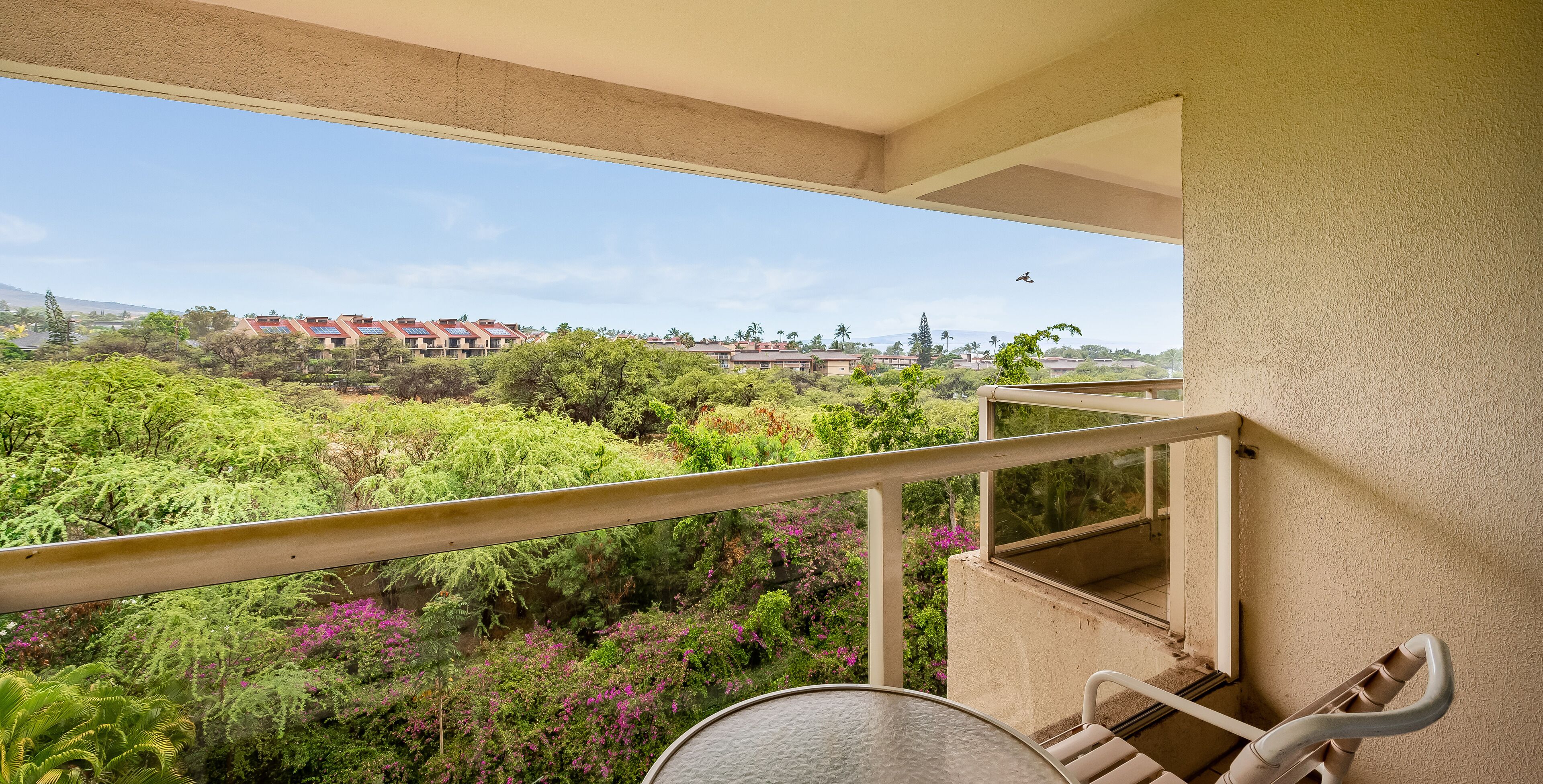 A balcony with a view of a lush garden and distant buildings.