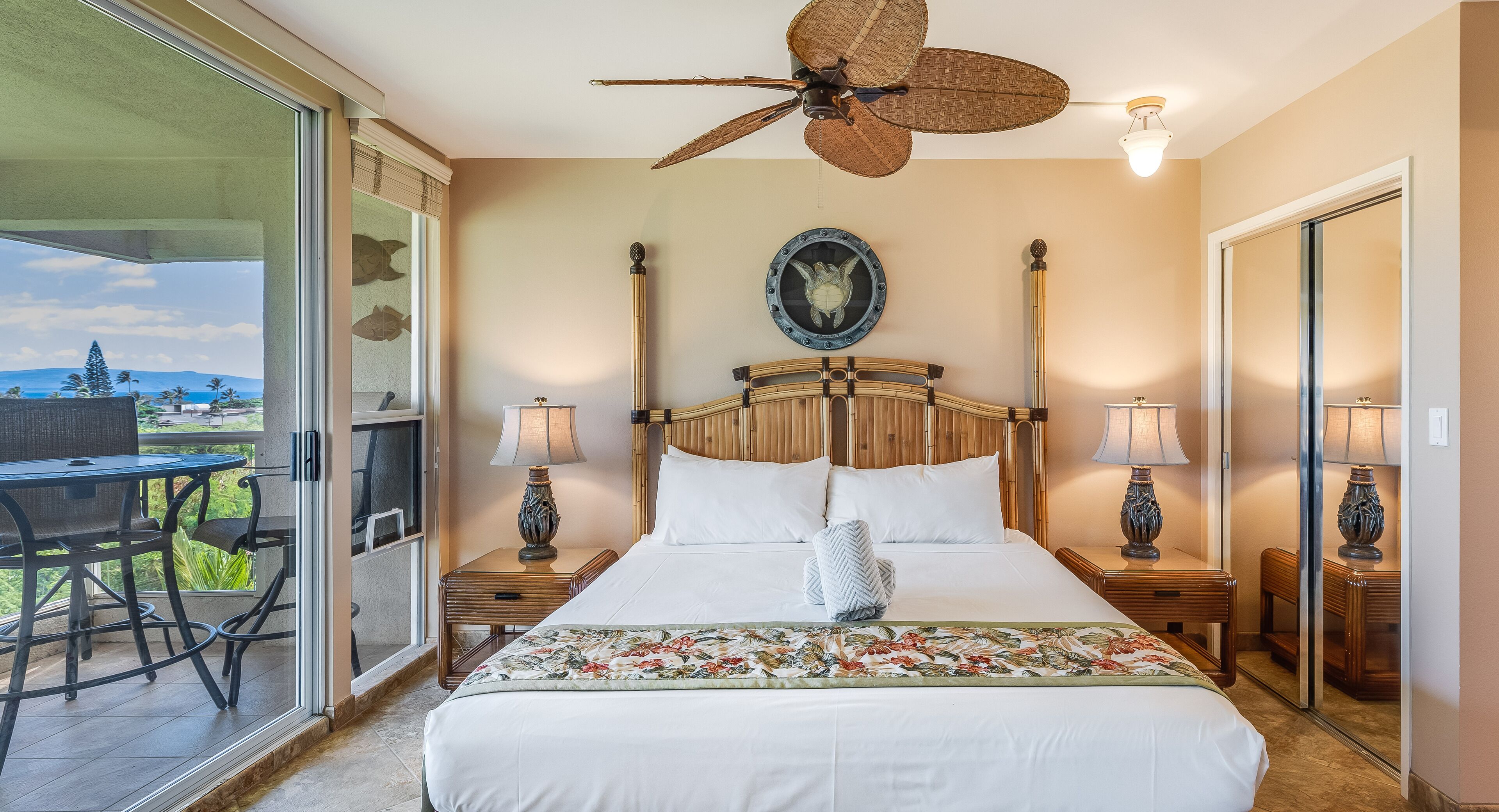 Habitación de hotel con una cama grande, dos mesitas de noche con lámparas, un ventilador de techo y vistas al exterior.