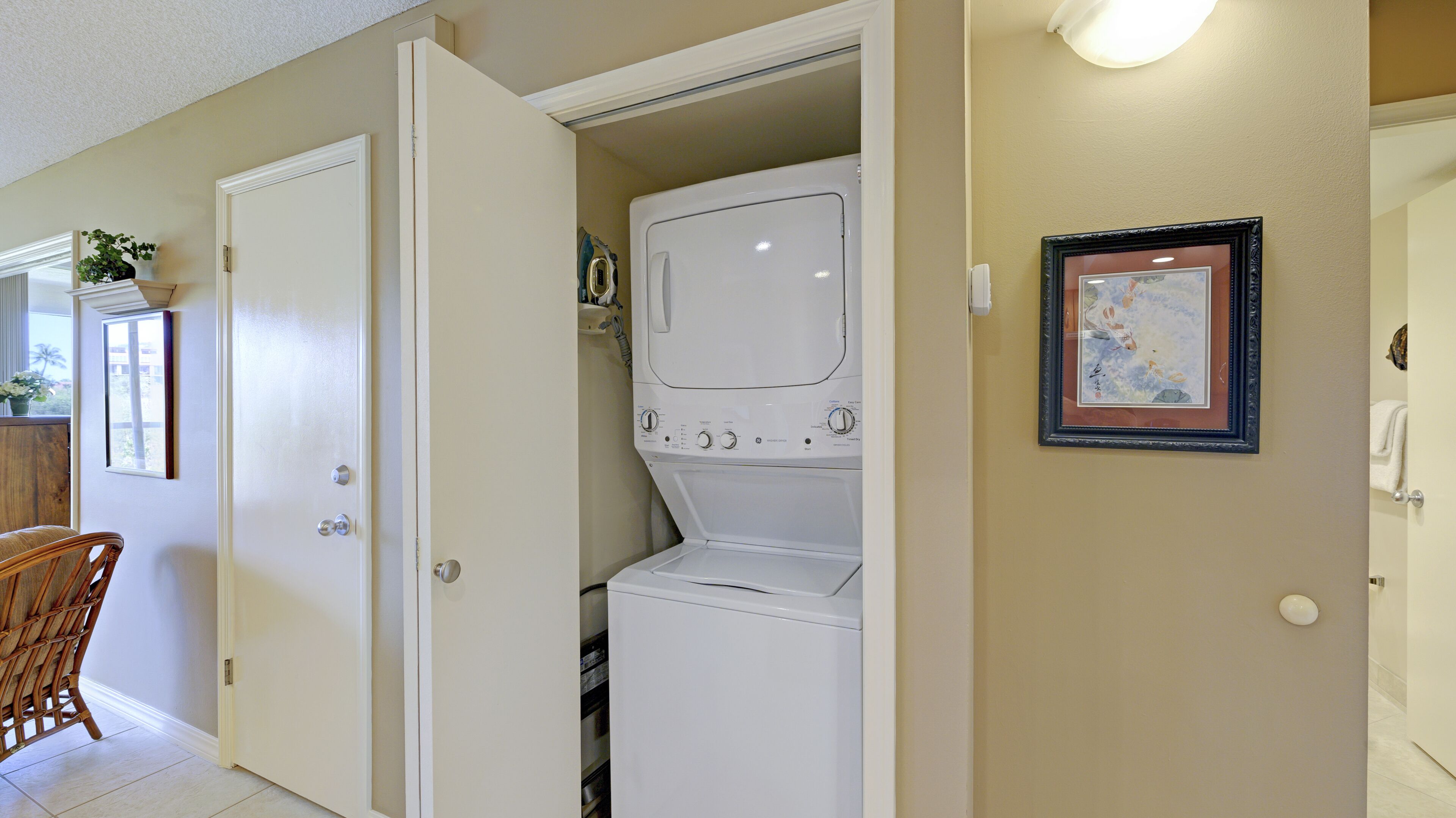 Une buanderie équipée d’un lave-linge et d’un sèche-linge, avec une chaise et un tableau encadré au mur.