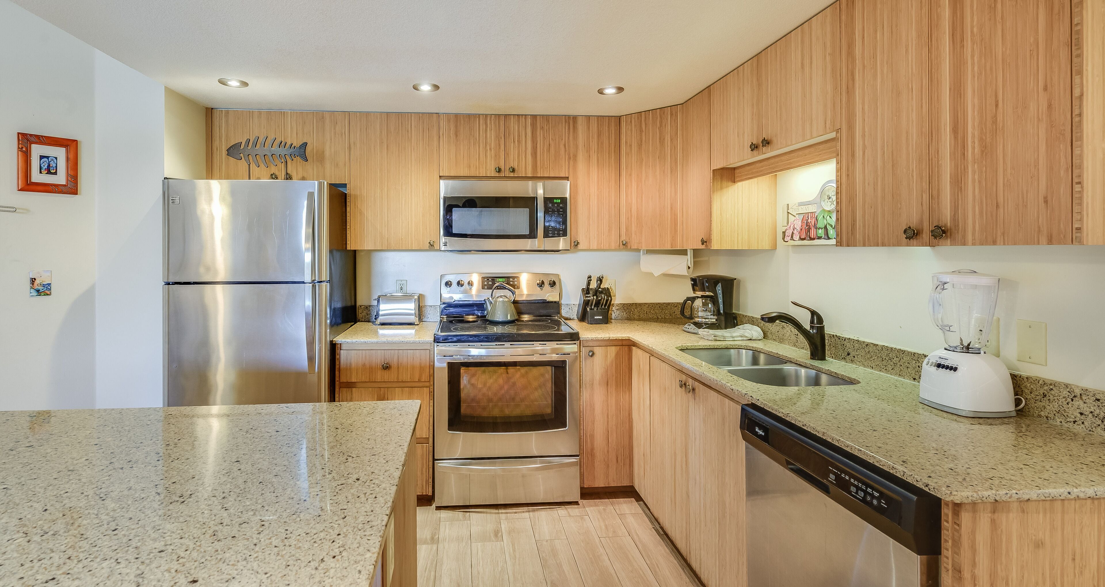 A modern kitchen with wooden cabinets, stainless steel appliances including a refrigerator, microwave, stove, and dishwasher, and granite countertops.